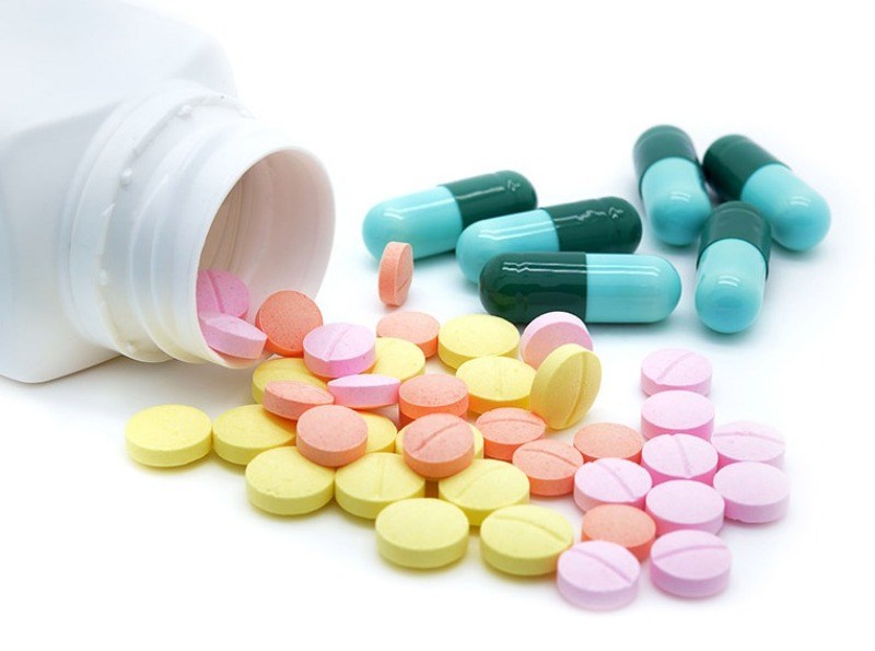 Different types of tablets spilling out of a supplement bottle.